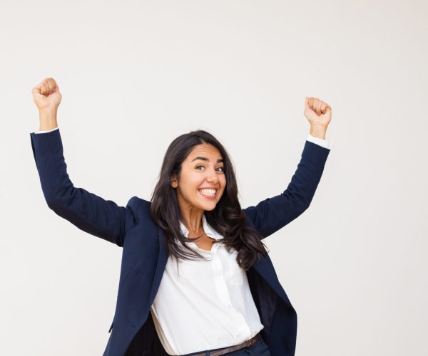 Excited young businesswoman triumphing. Happy young woman in formal wear shaking fists and smiling at camera isolated on grey background. Success concept